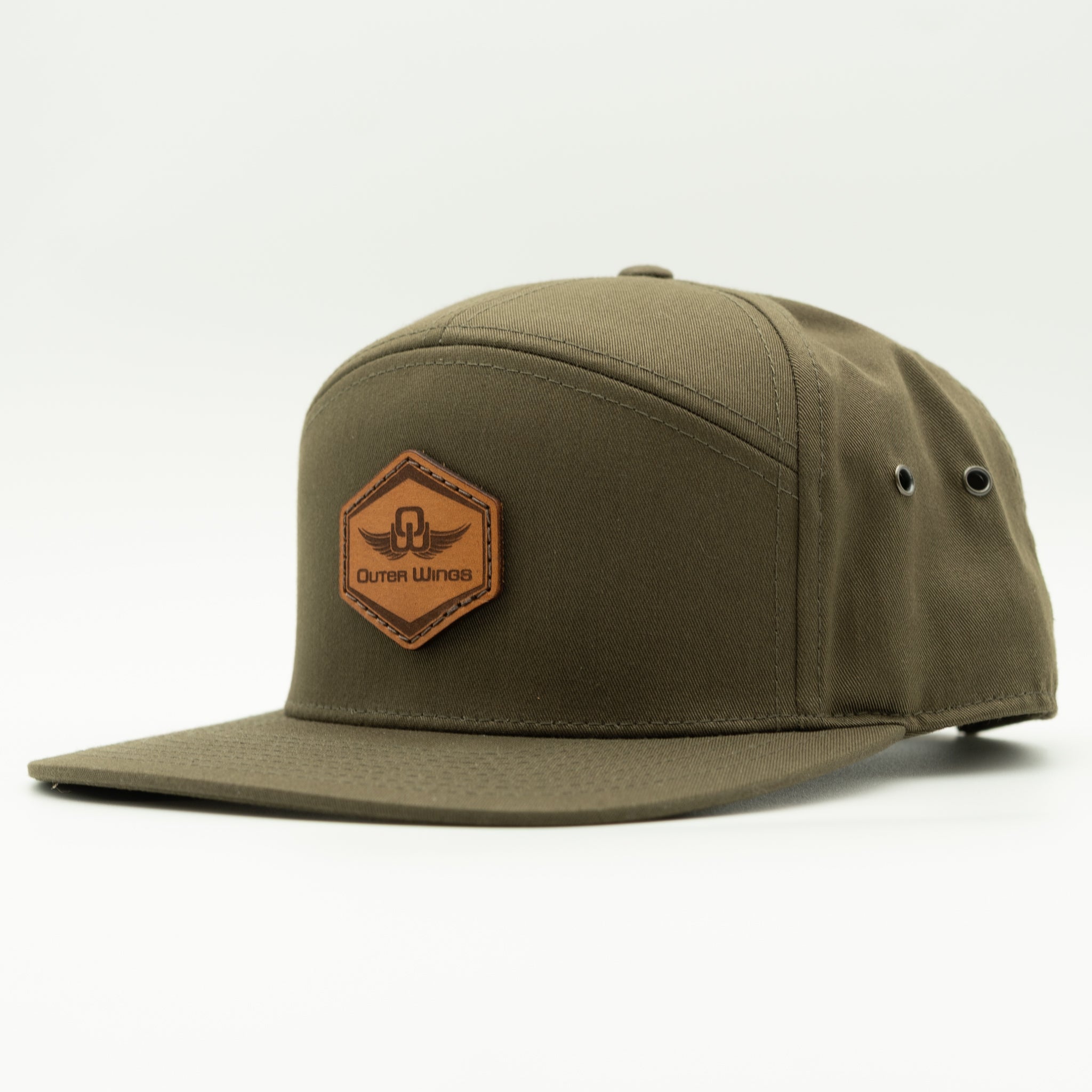An olive green snapback cap with a brown leather hexagonal patch on the front featuring the brand name 'Outer Wings'.
Color: Olive
