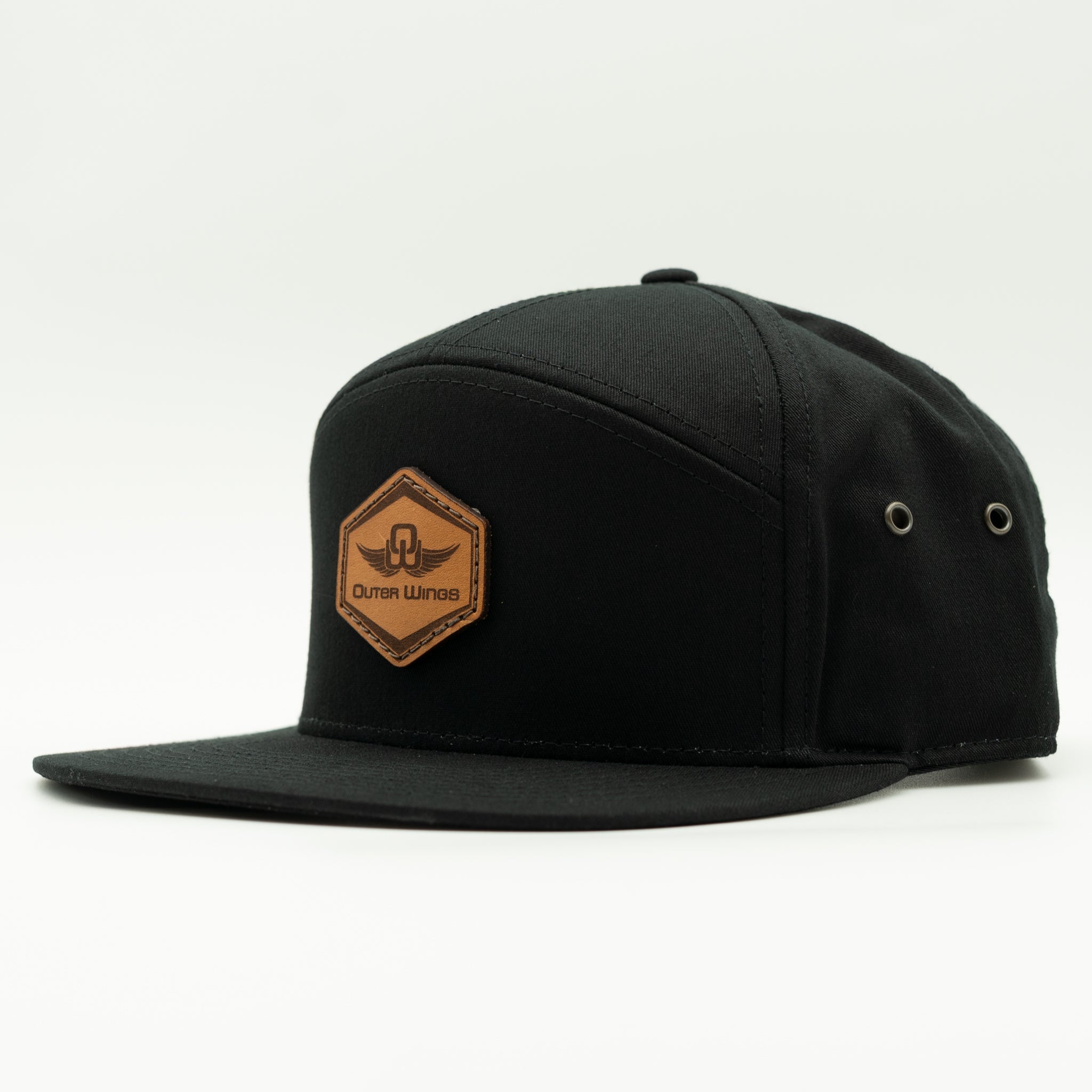 A black flat-brim cap with a brown hexagonal patch on the front featuring the brand name 'Outer Wings' and a winged logo, photographed on a clean white background.
Color: Black