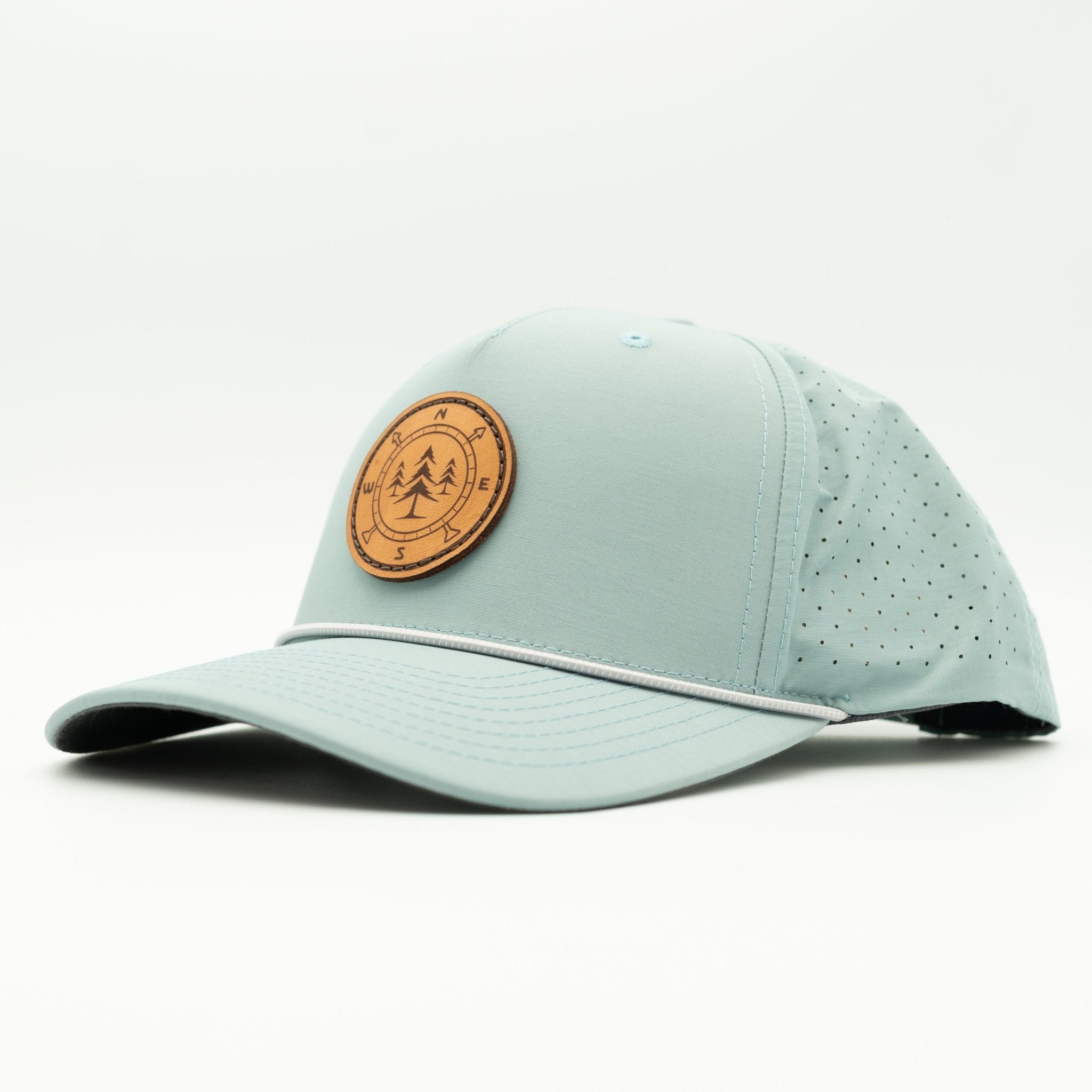 A light blue-green performance baseball cap with a curved brim, featuring a circular brown real leather sewn patch on the front with a tree logo, and perforated side panels.
Color: Smoke Blue