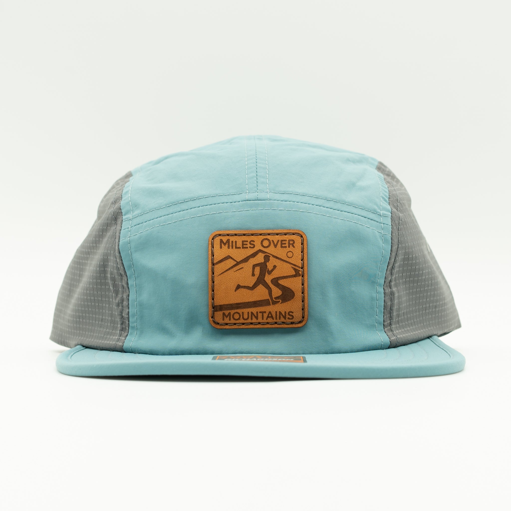 A light blue and gray 5-panel trucker hat with a brown leather patch on the front that reads 'Miles Over Mountains'.
Color: Smoke Blue/Charcoal