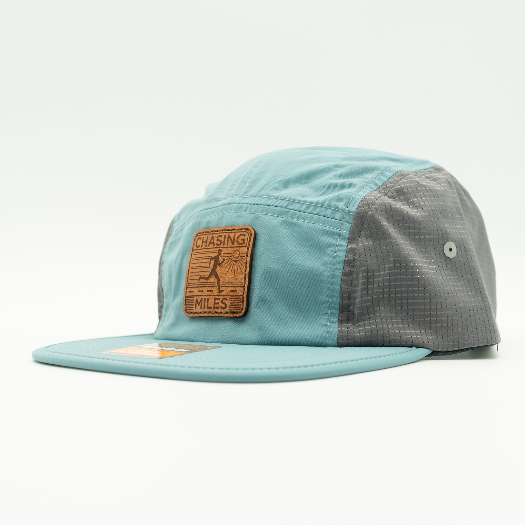 A light blue and gray 5-panel cap with a brown leather patch on the front that reads 'CHASING MILES'.
Color: Smoke Blue/Charcoal