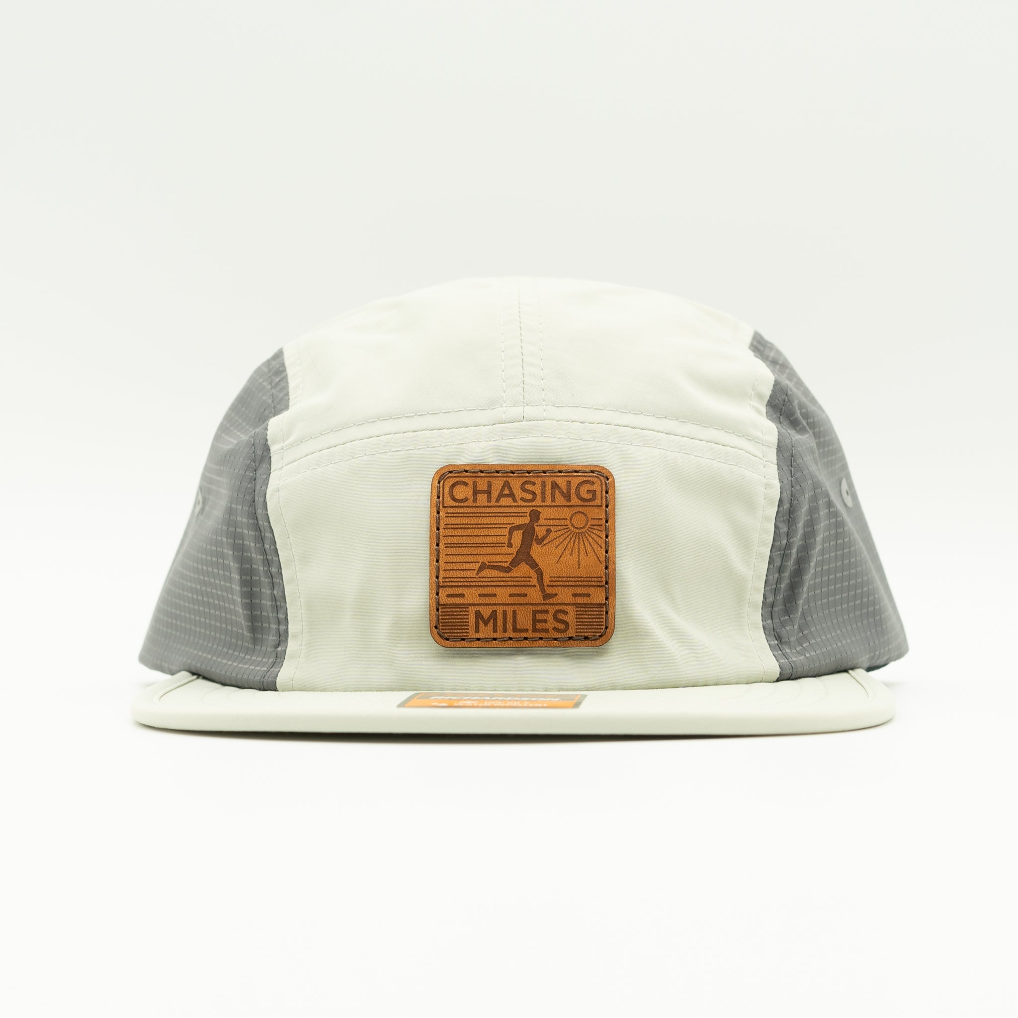 A 5-panel running cap with an off-white front panel and brim, gray mesh side panels, and a brown leather patch on the front that reads 'CHASING MILES'.
Color: Light Jade/Charcoal