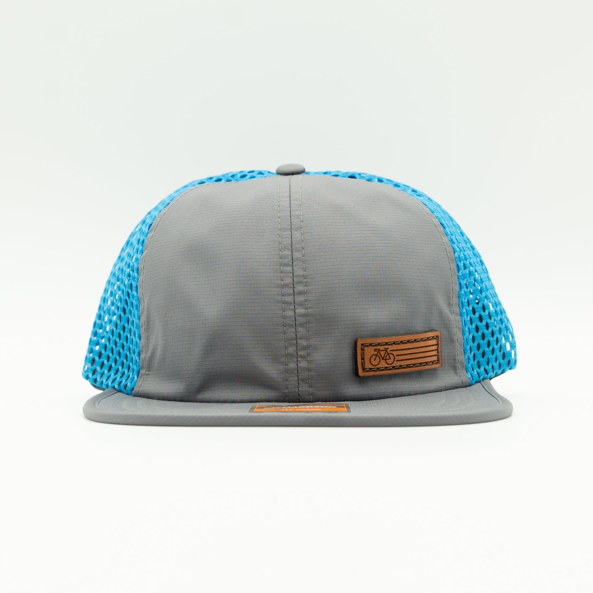 A gray flat-brim trucker cap with bright blue mesh side and back panels, featuring a brown leather patch on the front with a bicycle logo.
Color: Charcoal/Cyan