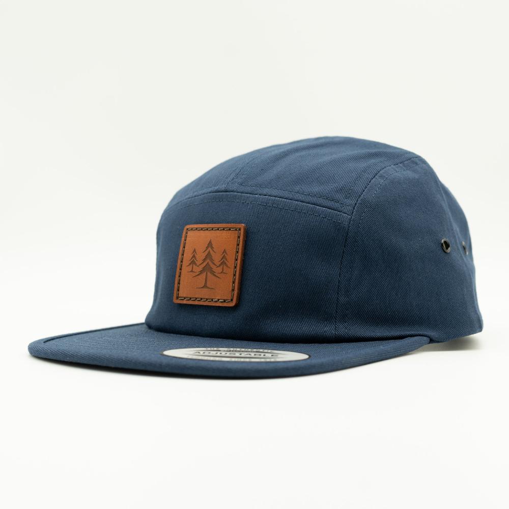Side view of navy Yupoong 7005 Three Lil Pines hat, highlighting the stitched leather pine tree patch, flat bill, and soft cotton construction.