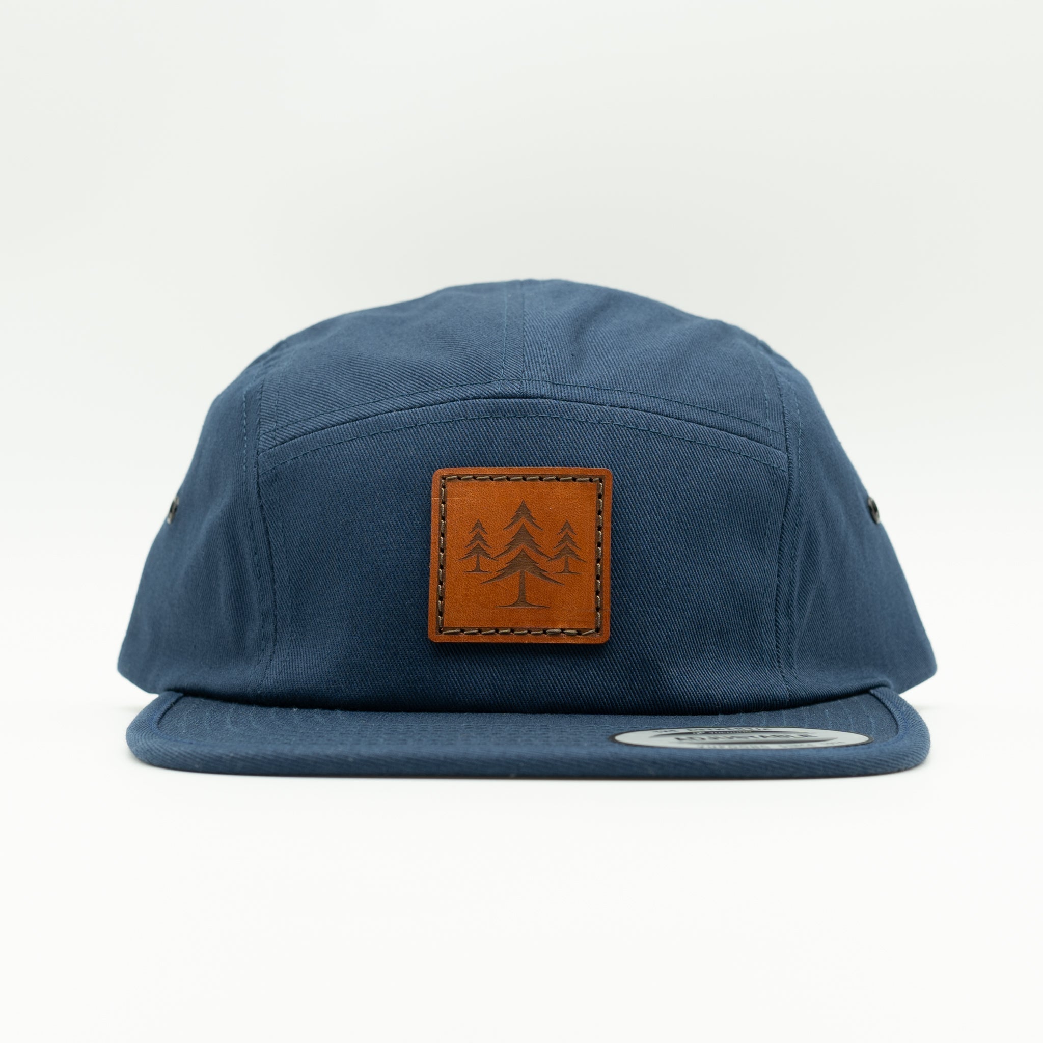 Front view of navy Three Lil Pines leather patch hat on Yupoong 7005, showing engraved pine tree patch, low-profile five panel crown, and flat bill.