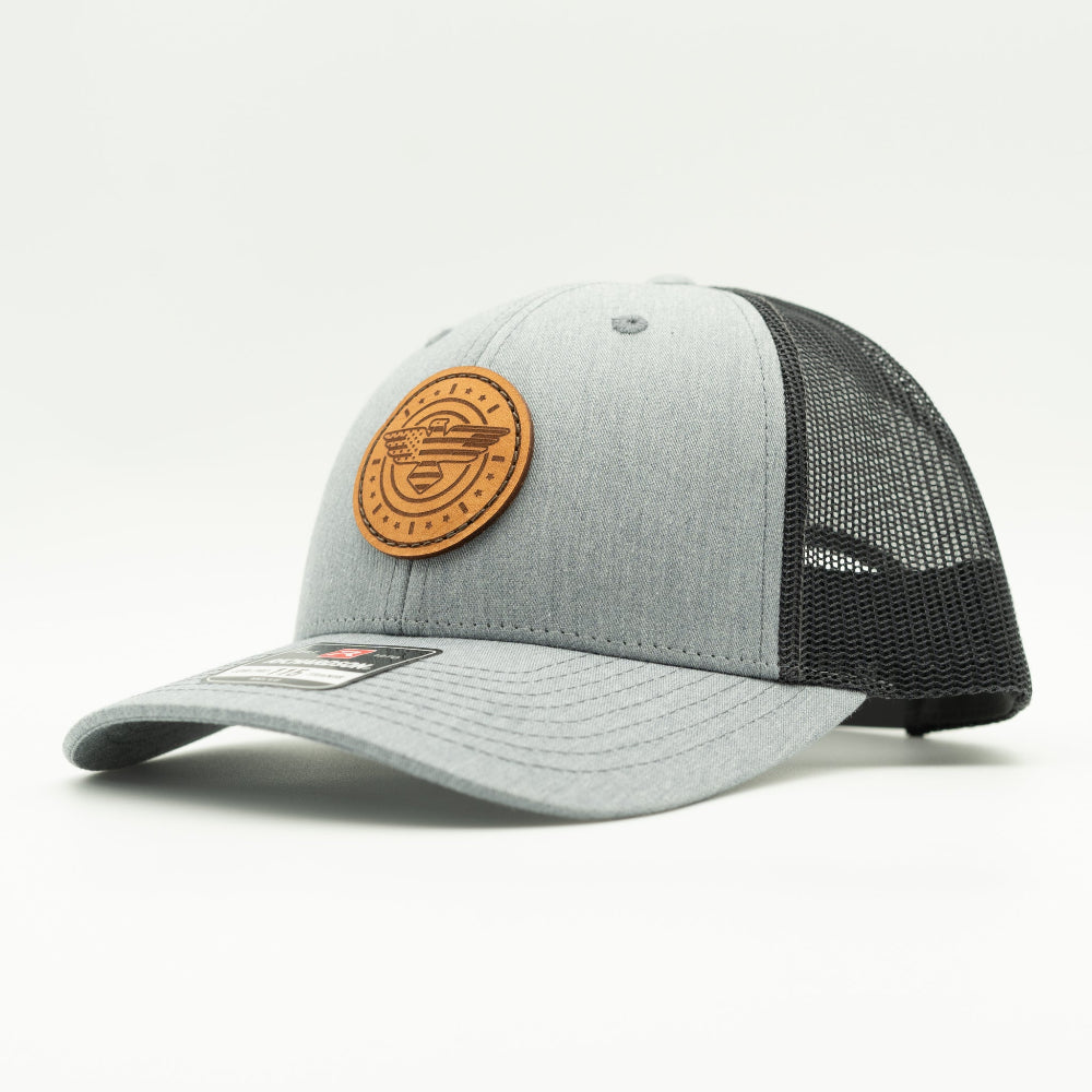 Side view of heather grey and charcoal Richardson 115 low profile trucker hat with American Eagle leather patch, showing shallow fit, curved bill, and charcoal mesh back.

Color: Heather Grey/Charcoal