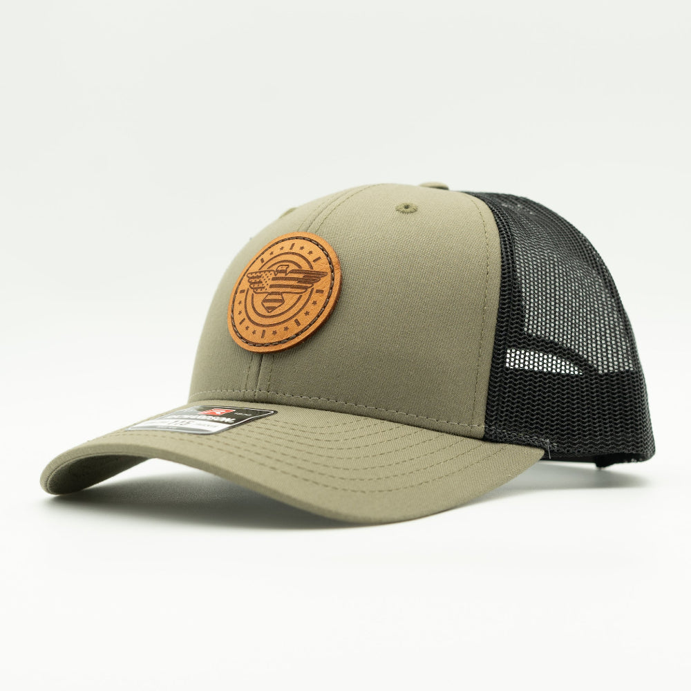 Side view of loden and black Richardson 115 low profile trucker hat with American Eagle leather patch, showing olive-toned front, curved bill, and black mesh back.

Color: Loden/Black