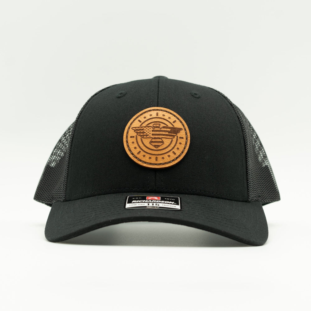Front view of solid black Richardson 115 low profile trucker hat with round American Eagle and flag leather patch, curved visor, and breathable black mesh back.

Color: Solid Black
