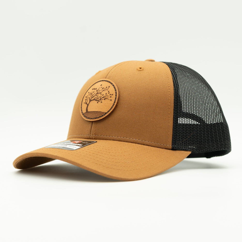 Side view of the Blossom Leather Patch Hat by Outer Wings in caramel/black, highlighting the hat’s low-profile fit, adjustable SnapBack, and the beautifully sewn Blossom leather patch. Ideal for adding a touch of elegance to your everyday look.