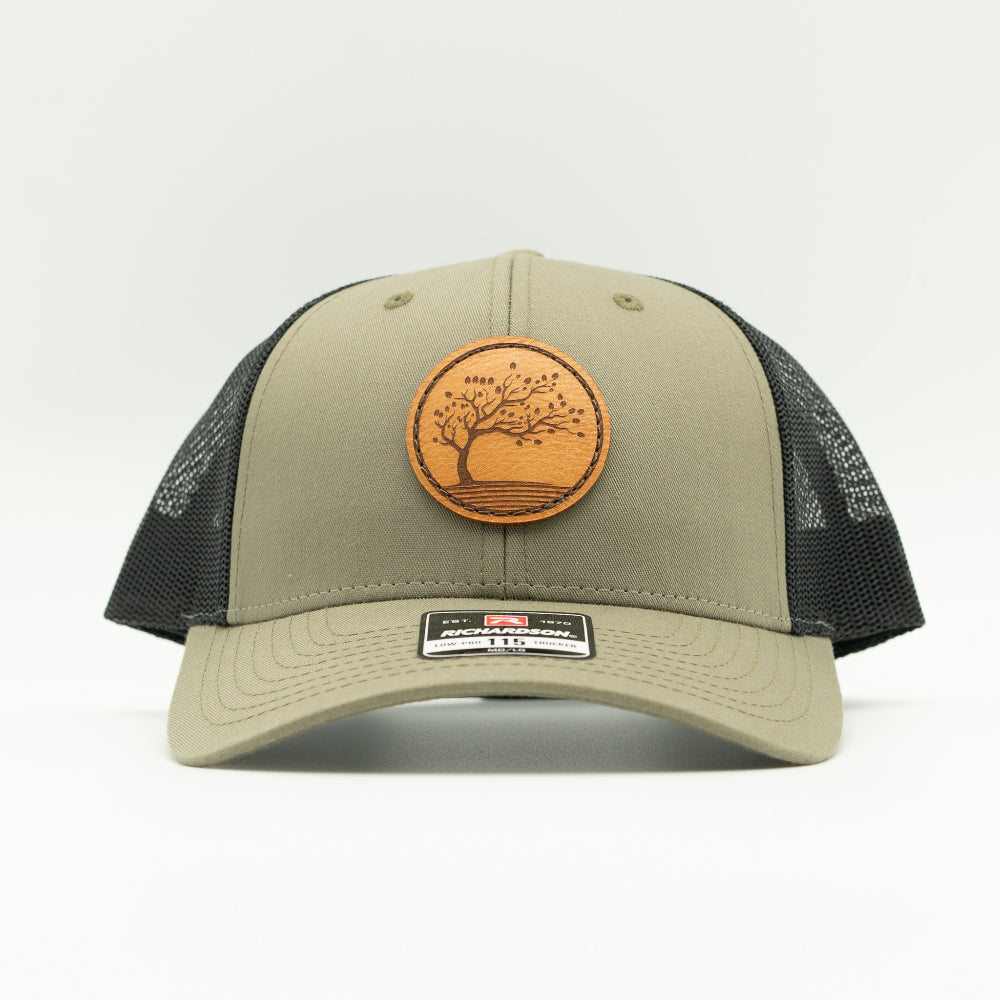 Front view of the Blossom Leather Patch Hat by Outer Wings in loden/black, highlighting the low-profile design, adjustable SnapBack, and the beautifully engraved Blossom leather patch. A perfect hat for those who love the outdoors and premium quality.