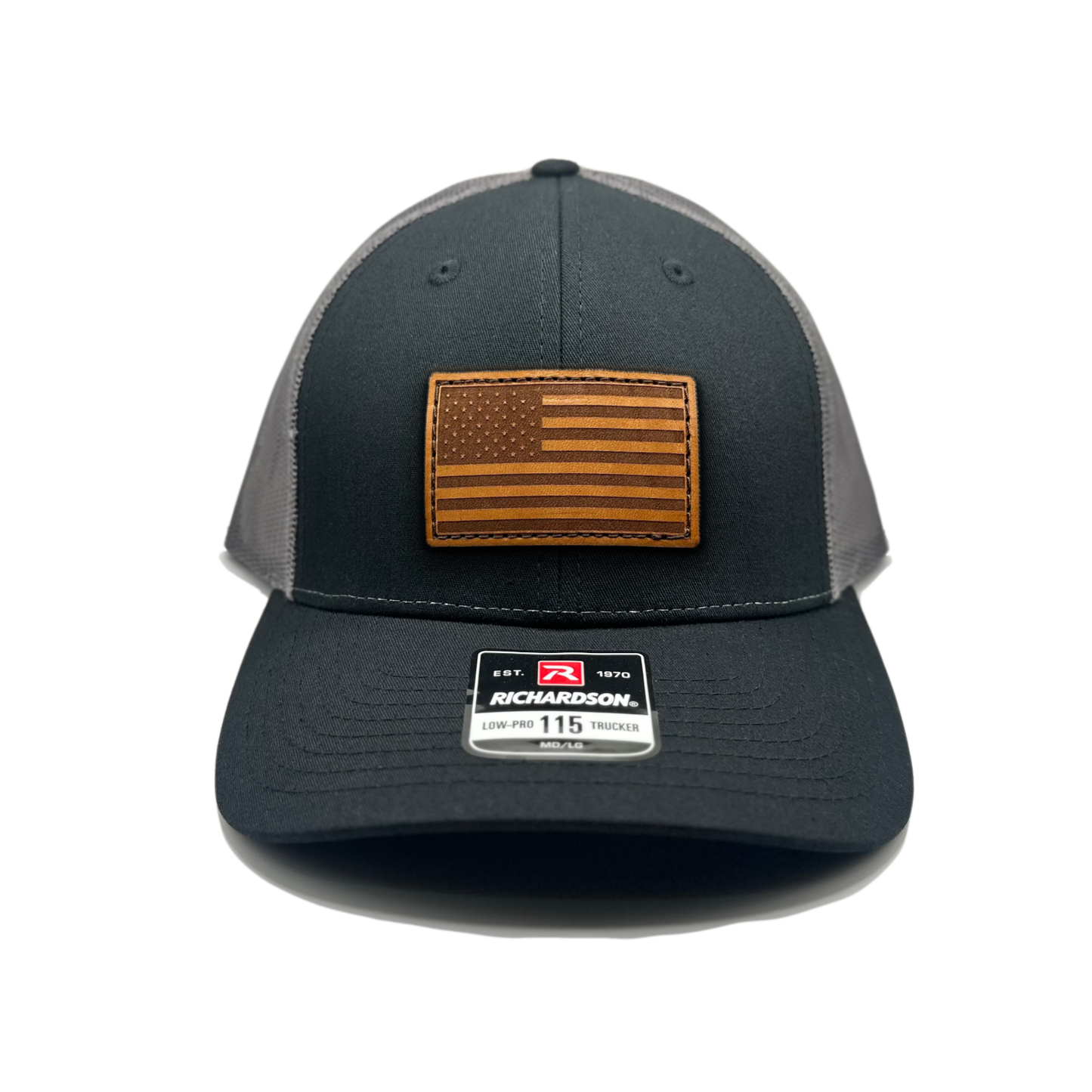 Image of a Black/Charcoal Richardson 115 hat with an American flag patch made of genuine leather, laser engraved and securely sewn onto the hat. The low profile trucker style hat is adjustable to fit small or M/L sizes, offering a versatile and fashionable accessory for any occasion."