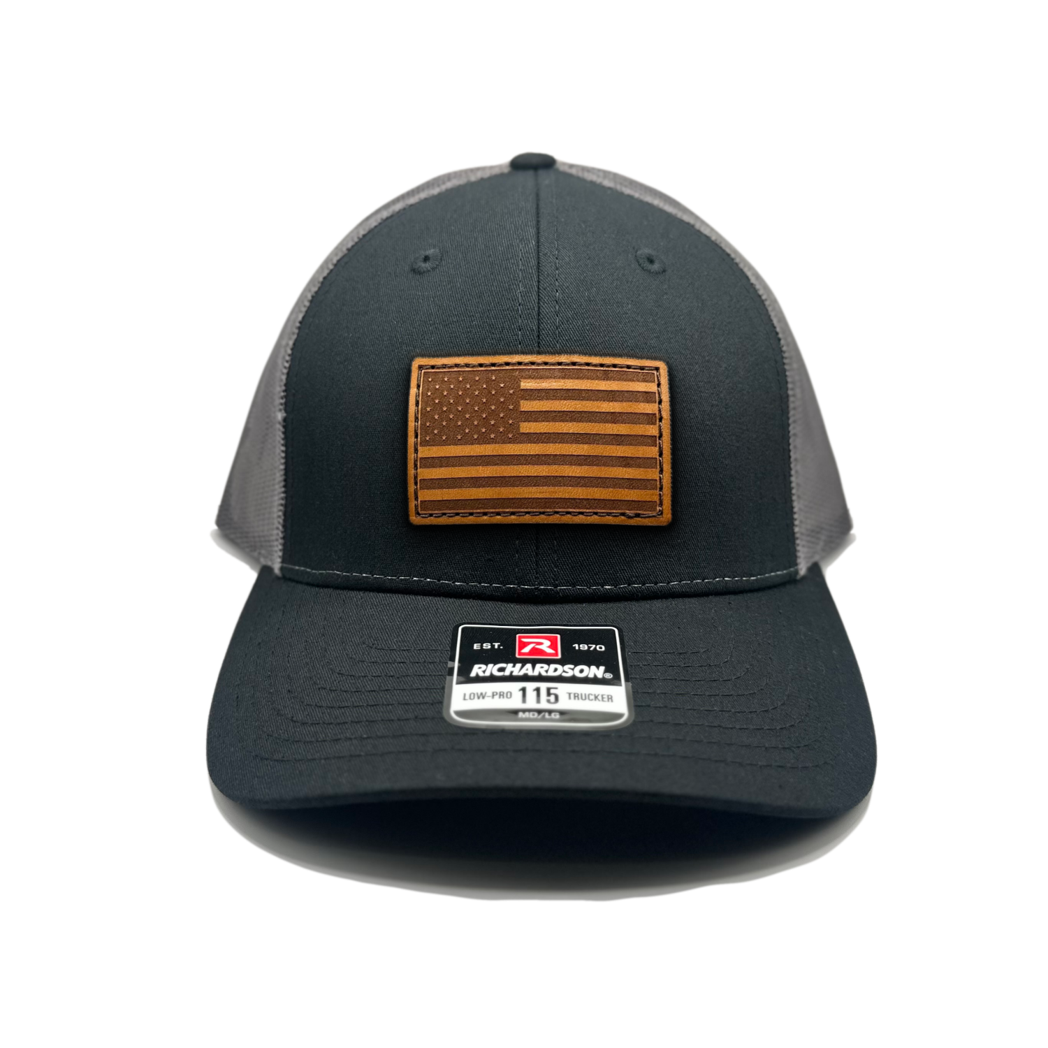 Image of a Black/Charcoal Richardson 115 hat with an American flag patch made of genuine leather, laser engraved and securely sewn onto the hat. The low profile trucker style hat is adjustable to fit small or M/L sizes, offering a versatile and fashionable accessory for any occasion."