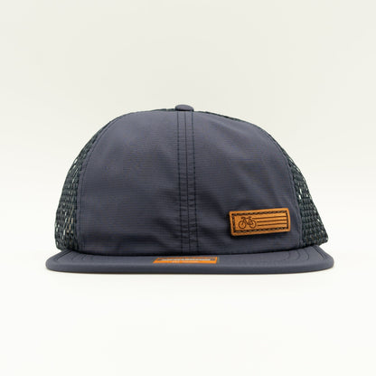 Front view of the Navy Fast Bike Hat, featuring the matching navy wide-set mesh back and adjustable quick-adjust pack webbing, with the Fast Bike leather patch visible from the side.