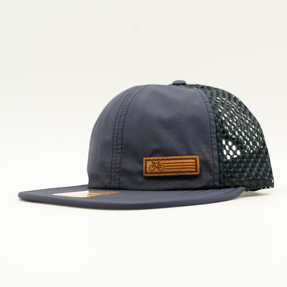 Side view of the Navy Fast Bike Hat, featuring the matching navy wide-set mesh back and adjustable quick-adjust pack webbing, with the Fast Bike leather patch visible from the side.