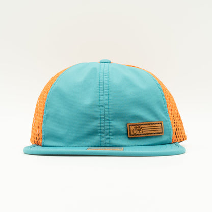 Front view of the Teal Fast Bike Hat, displaying the vibrant orange accents and wide-set mesh back, with the Fast Bike leather patch visible from the side.