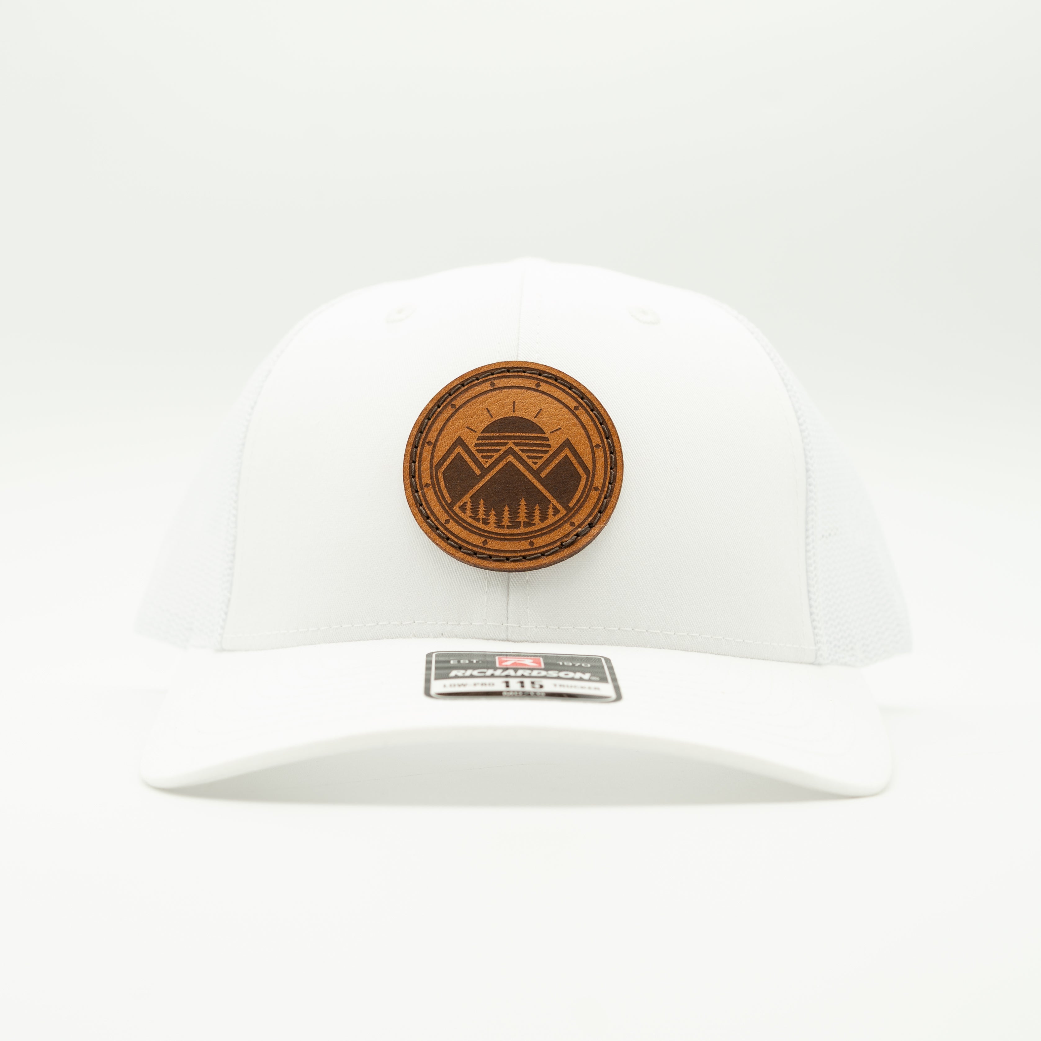 A white structured baseball cap with a circular brown leather mountain emblem on the front and a small black-and-white size/brand patch on the brim, photographed against a clean white background.

Color: Solid White