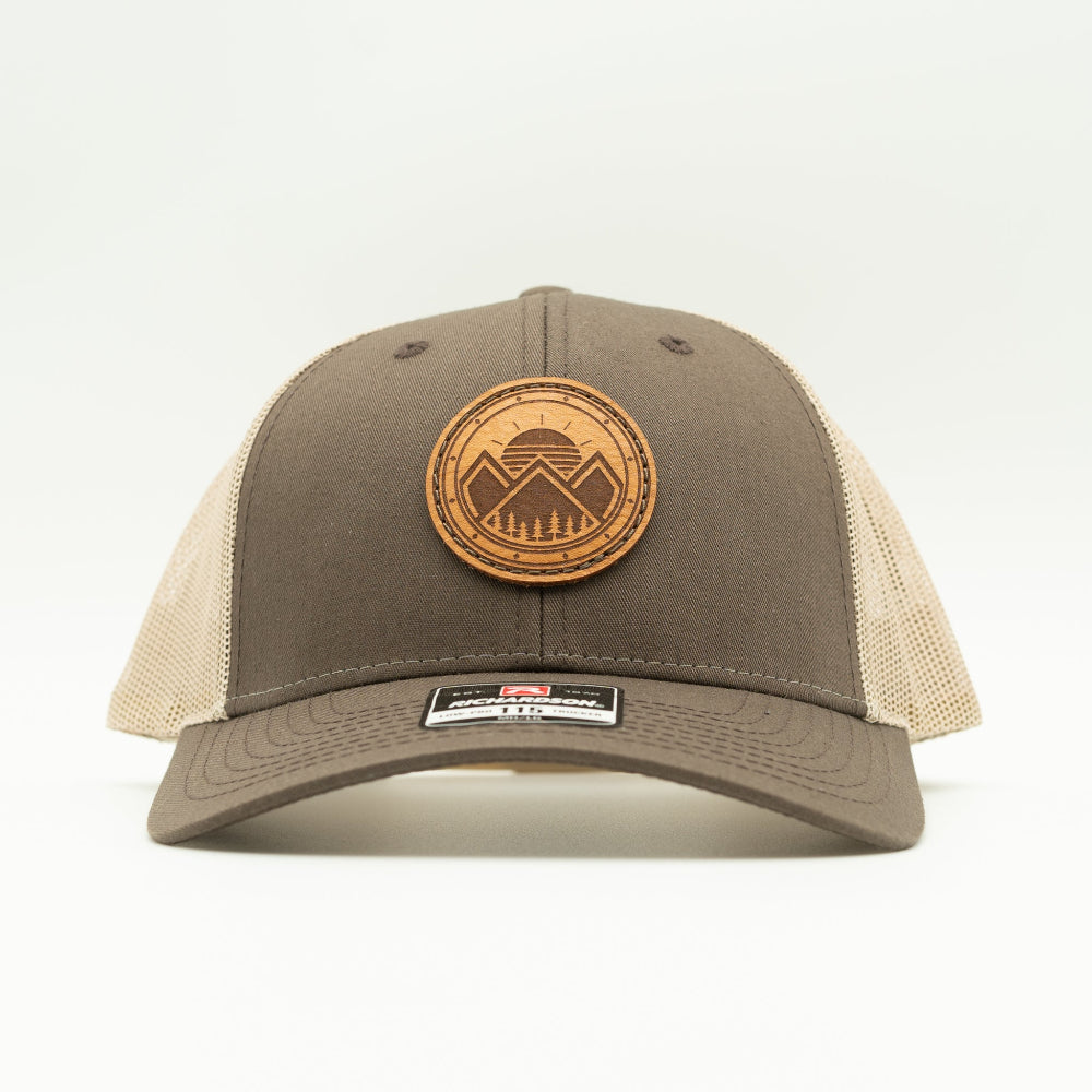 Front view of the Modern Mountains Leather Patch Hat in Brown/Khaki, highlighting the structured profile, breathable mesh back, and adjustable SnapBack closure. The genuine leather patch with a modern mountains and sunset design adds a distinctive touch to the hat’s style.