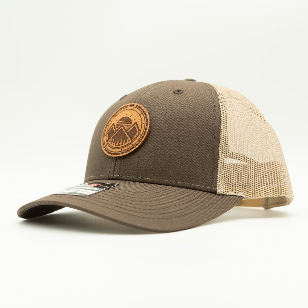 Side view of the Modern Mountains Leather Patch Hat in Brown/Khaki, highlighting the structured profile, breathable mesh back, and adjustable SnapBack closure. The genuine leather patch with a modern mountains and sunset design adds a distinctive touch to the hat’s style.