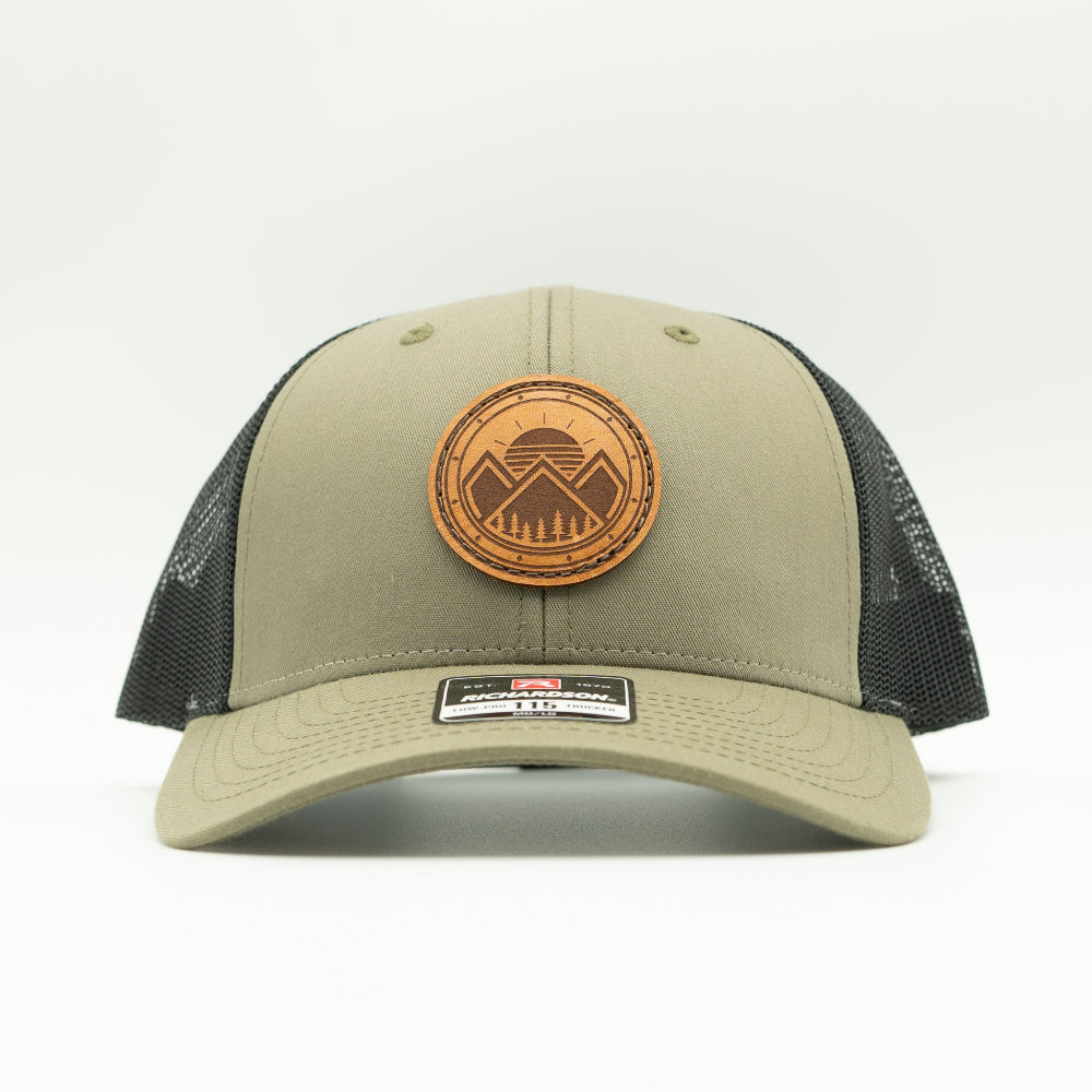 Front view of the Modern Mountains Leather Patch Hat in Loden/Black, showing the hat’s low-profile structure, pre-curved visor, and adjustable SnapBack. The leather patch features a modern mountains and sunset design, perfect for those who love the outdoors.