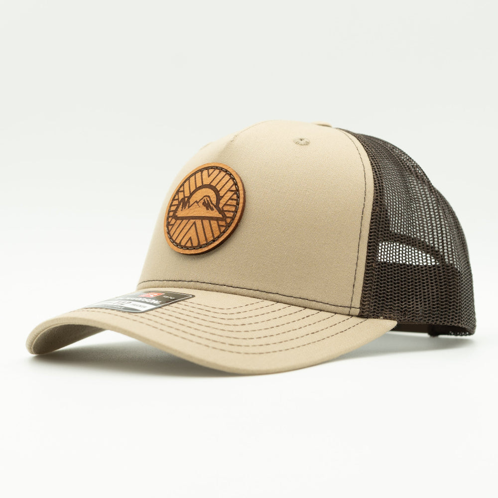 Side view of the Mosaic Sunset Leather Patch Hat by Outer Wings in khaki/coffee, showing the mid-profile structure of the Richardson 112FP. The detailed leather patch with a Mosaic Sunset engraving adds a rugged, artistic flair to this custom leather patch hat, perfect for outdoor enthusiasts. The mesh back and adjustable Snap-Back ensure a comfortable and secure fit.