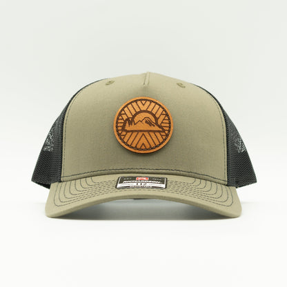 Front view of the Mosaic Sunset Leather Patch Hat by Outer Wings in loden/black, highlighting the structured mid-profile design of the Richardson 112FP. The side showcases the unique laser-engraved leather patch with the Mosaic Sunset design, adding a distinctive look to this custom leather patch hat. Ideal for outdoor adventures, the hat features a breathable mesh back and adjustable Snap-Back for comfort and versatility.