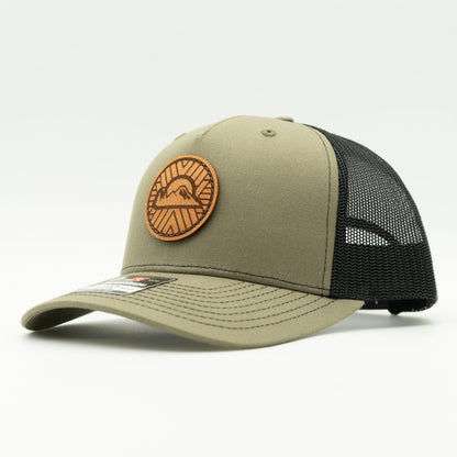 Side view of the Mosaic Sunset Leather Patch Hat by Outer Wings in loden/black, highlighting the structured mid-profile design of the Richardson 112FP. The side showcases the unique laser-engraved leather patch with the Mosaic Sunset design, adding a distinctive look to this custom leather patch hat. Ideal for outdoor adventures, the hat features a breathable mesh back and adjustable Snap-Back for comfort and versatility.