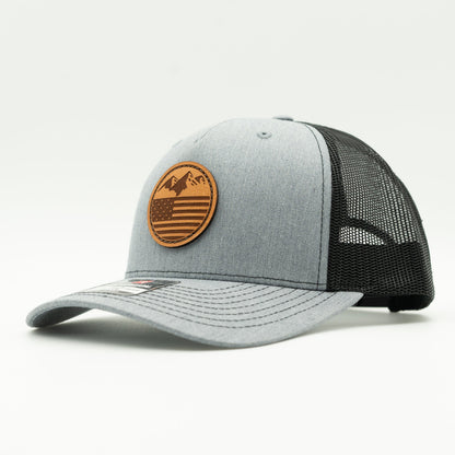 Side view of the Mountain Flag leather patch hat on Richardson 112FP in Heather/Black, highlighting the flat bill, adjustable snapback, and seamless front panel. The perfect custom leather patch hat for outdoor activities.