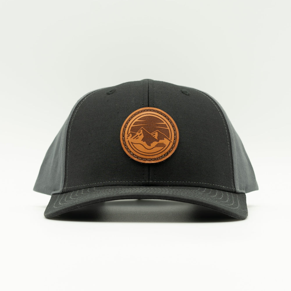 Front view of the Mountain Lake leather patch hat on Richardson 312 in Black/Charcoal, featuring a six-panel, mid-profile design with a pre-curved visor and real leather patch showcasing the Mountain Lake design. Ideal for outdoor enthusiasts.