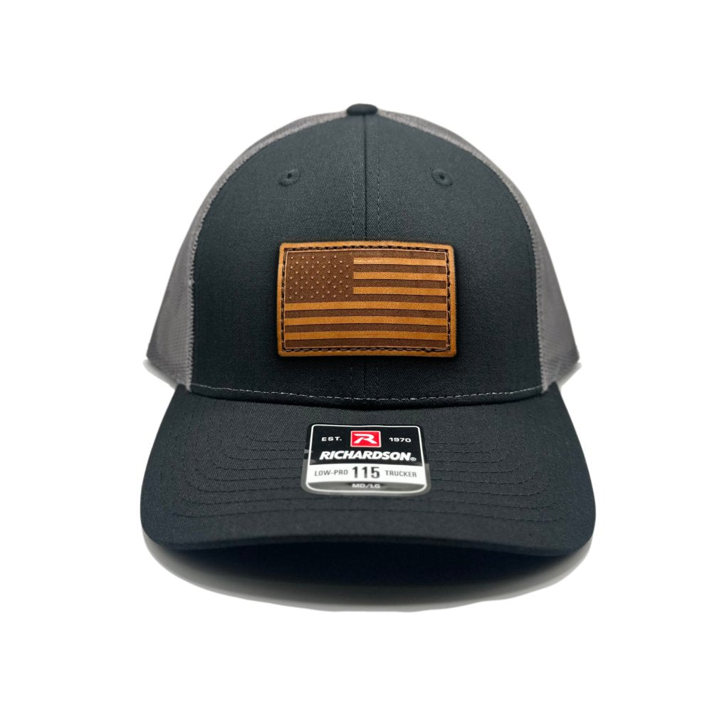 Black/Charcoal American Flag Hat by Richardson 115 showcasing the genuine leather American Flag patch, laser-engraved and hand-sewn, on a black and charcoal trucker hat.