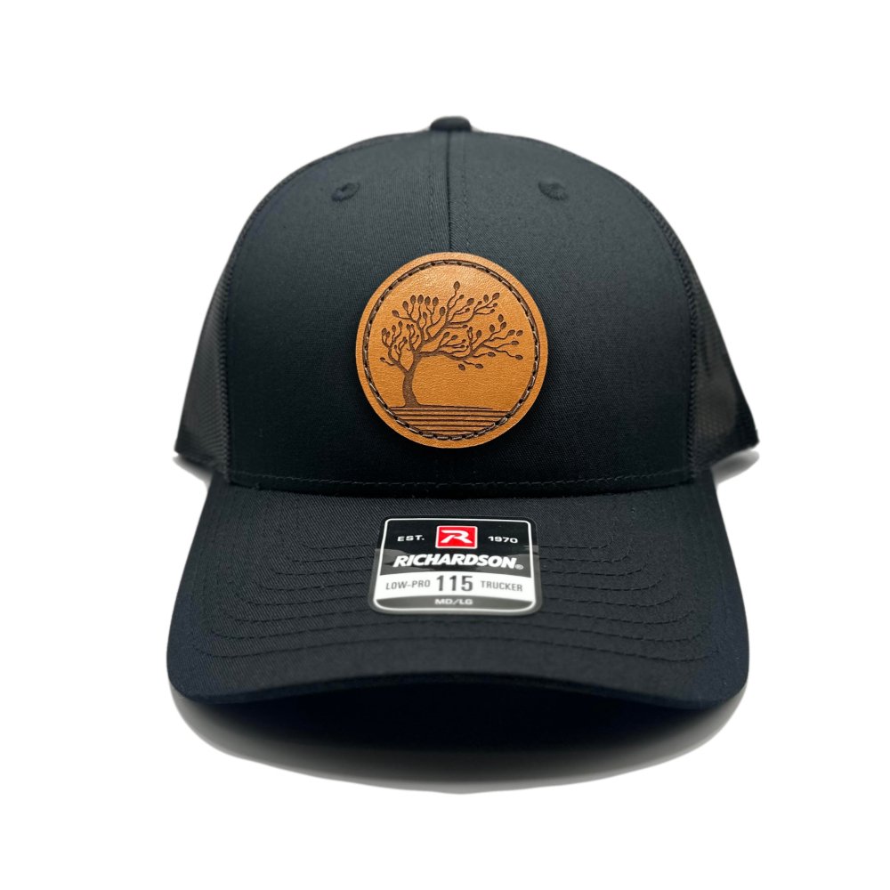 Front view of the Blossom Leather Patch Hat by Outer Wings in black/black, featuring a low-profile Richardson 115 hat with a square leather patch showcasing the Blossom design. The hat is made from durable materials with a structured build and adjustable SnapBack closure, offering a sleek and stylish fit