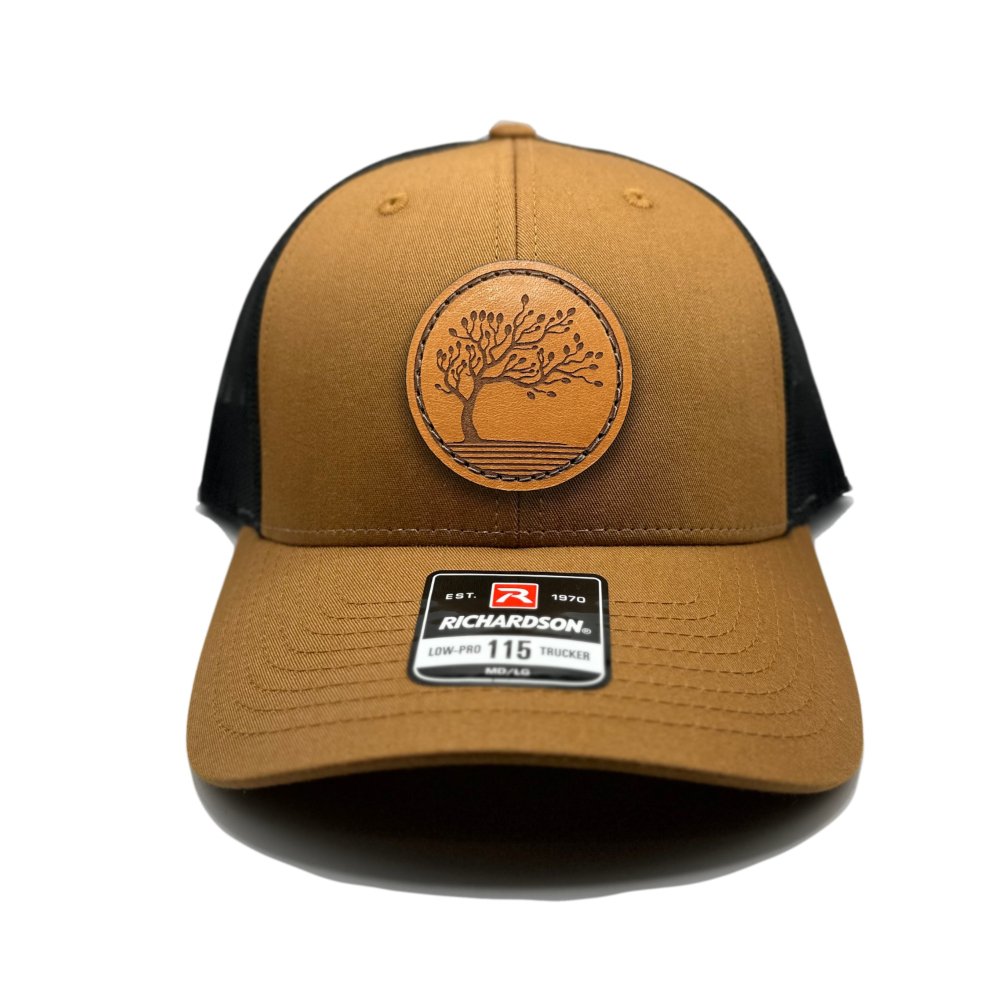 Front view of the Blossom Leather Patch Hat by Outer Wings in caramel/black, featuring a low-profile Richardson 115 hat with a leather patch of the Blossom design. The caramel front with a black mesh back offers a unique and eye-catching style.