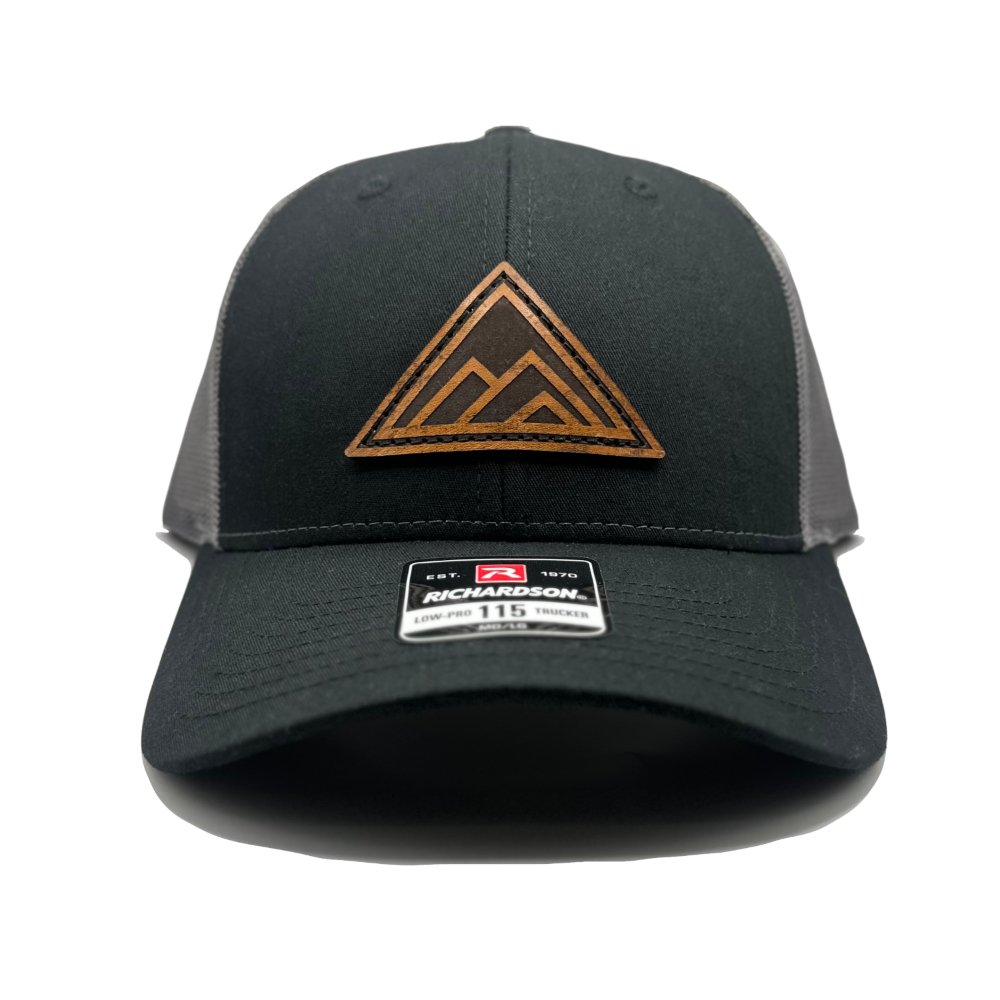 Front view of the Dark Mountain Leather Patch Hat by Outer Wings in black/charcoal on the low-profile Richardson 115. Featuring a sleek circular leather patch with the Dark Mountain design, this hat is made from durable fabric with a structured build and an adjustable SnapBack closure.