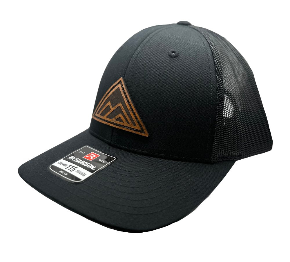 Side view of the Dark Mountain Leather Patch Hat by Outer Wings in black/black on the Richardson 115, showcasing the low-profile structure, comfortable fit, and the precisely sewn circular Dark Mountain leather patch. Perfect for a sleek, modern look.