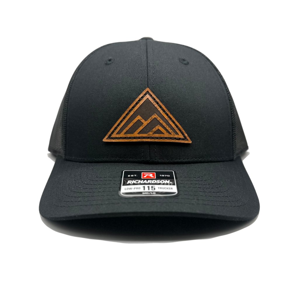 Front view of the Dark Mountain Leather Patch Hat by Outer Wings in black/black on the low-profile Richardson 115. The hat features a circular leather patch with the Dark Mountain design, laser engraved and meticulously sewn for durability. Made from water-resistant materials with a structured build and adjustable SnapBack closure.