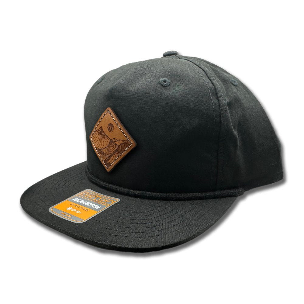 Side view of the Desert Mountain Leather Patch Hat by Outer Wings in black/black on the Richardson 256, emphasizing the low-profile, five-panel design, classic rope detail, and the precisely sewn Desert Mountain leather patch. Perfect for a sleek, stylish look with outdoor functionality.