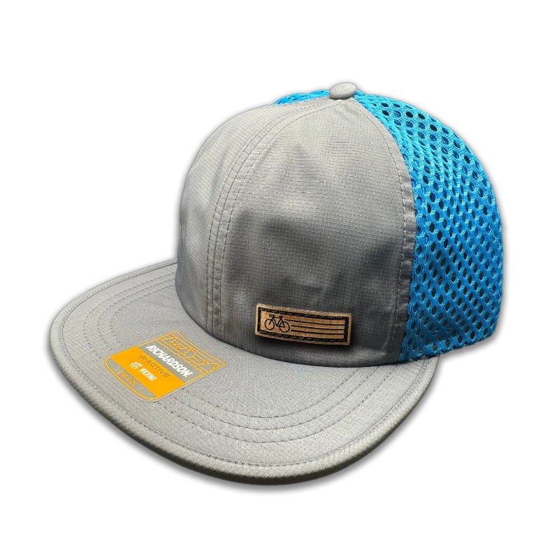 Side view of the Charcoal Fast Bike Hat, highlighting the contrast cyan accents and wide-set mesh back, with the Fast Bike leather patch visible from the side.