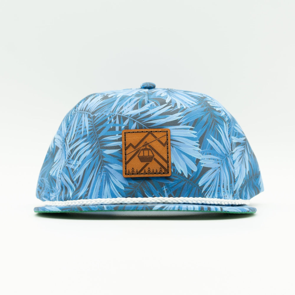 Front view of the Gondola Hat in Blue Pine by Outer Wings, displaying a genuine leather patch with detailed winter-themed designs including skiers, ski lifts, and pine trees. Crafted on an Imperial Umpqua rope hat with a structured mid-profile, moisture-wicking sweatband, and adjustable leather strap