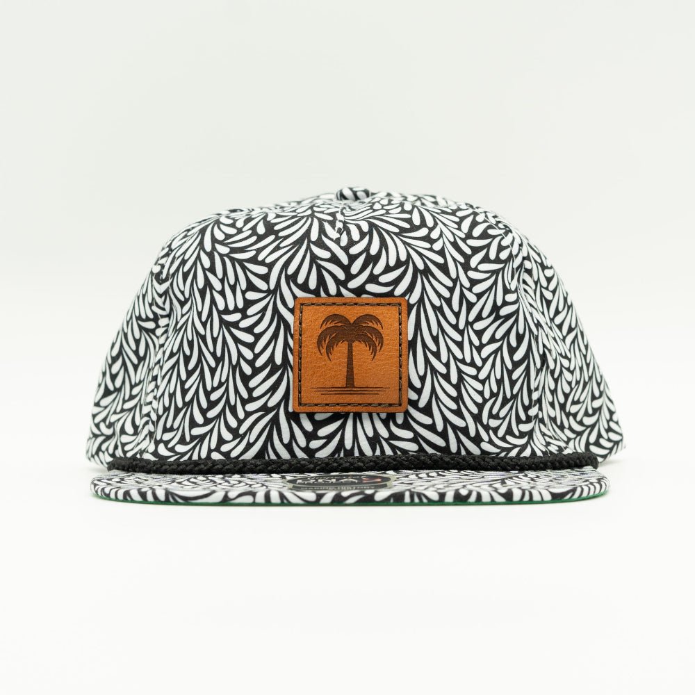 A flat-brim snapback cap featuring a black and white leaf pattern, with a brown leather patch on the front displaying a palm tree logo.

Color: Throwback Black