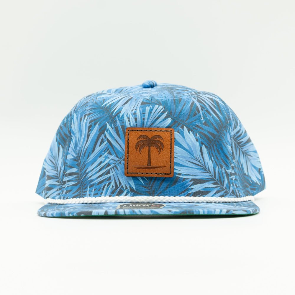 A blue and light blue tropical palm leaf pattern snapback cap with a brown leather patch featuring an embossed palm tree on the front, set against a plain white background.

Color: Blue Hawaiian