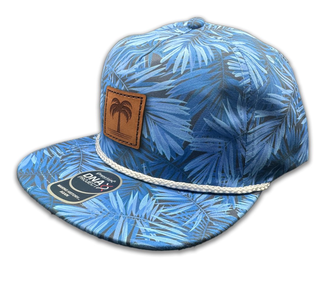 Side view of the Island Breeze Hat in Blue Hawaiian, showcasing the blue tropical-themed print, structured design, and adjustable leather strap. The hat includes a distinctive palm tree-engraved leather patch, perfect for capturing the essence of the islands.