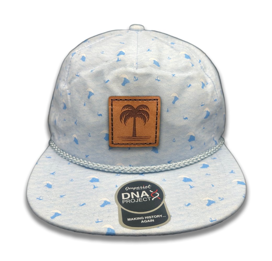 Front view of the Island Breeze Hat in Blue Waves by Outer Wings, featuring a hand-sewn full-grain leather patch with a palm tree engraving. This hat boasts a blue ocean wave-themed print on the Imperial DNA010 Aloha Rope Hat, with a structured five-panel, mid-profile design and an adjustable leather strap.