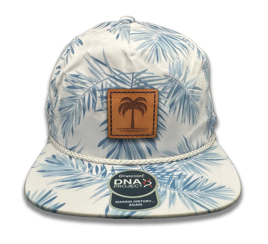 Front view of the Island Breeze Hat in Floral Mist by Outer Wings, featuring a hand-sewn leather patch with an engraved palm tree design. Crafted on the Imperial DNA010 Aloha Rope Hat, it presents a unique floral-themed print with a structured five-panel, mid-profile and adjustable leather strap.