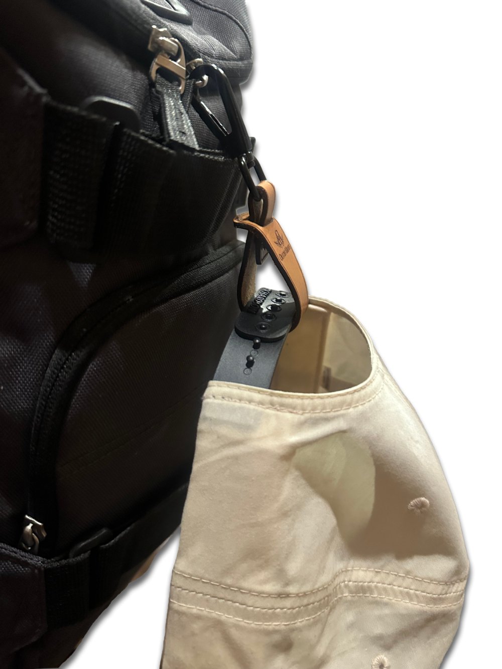Side view of the Outer Wings leather hat clip in use, showing a hat hanging from a backpack. The clip's robust design with Chicago rivets and quick link keychain ensures a secure hold, making it ideal for outdoor activities and travel.
