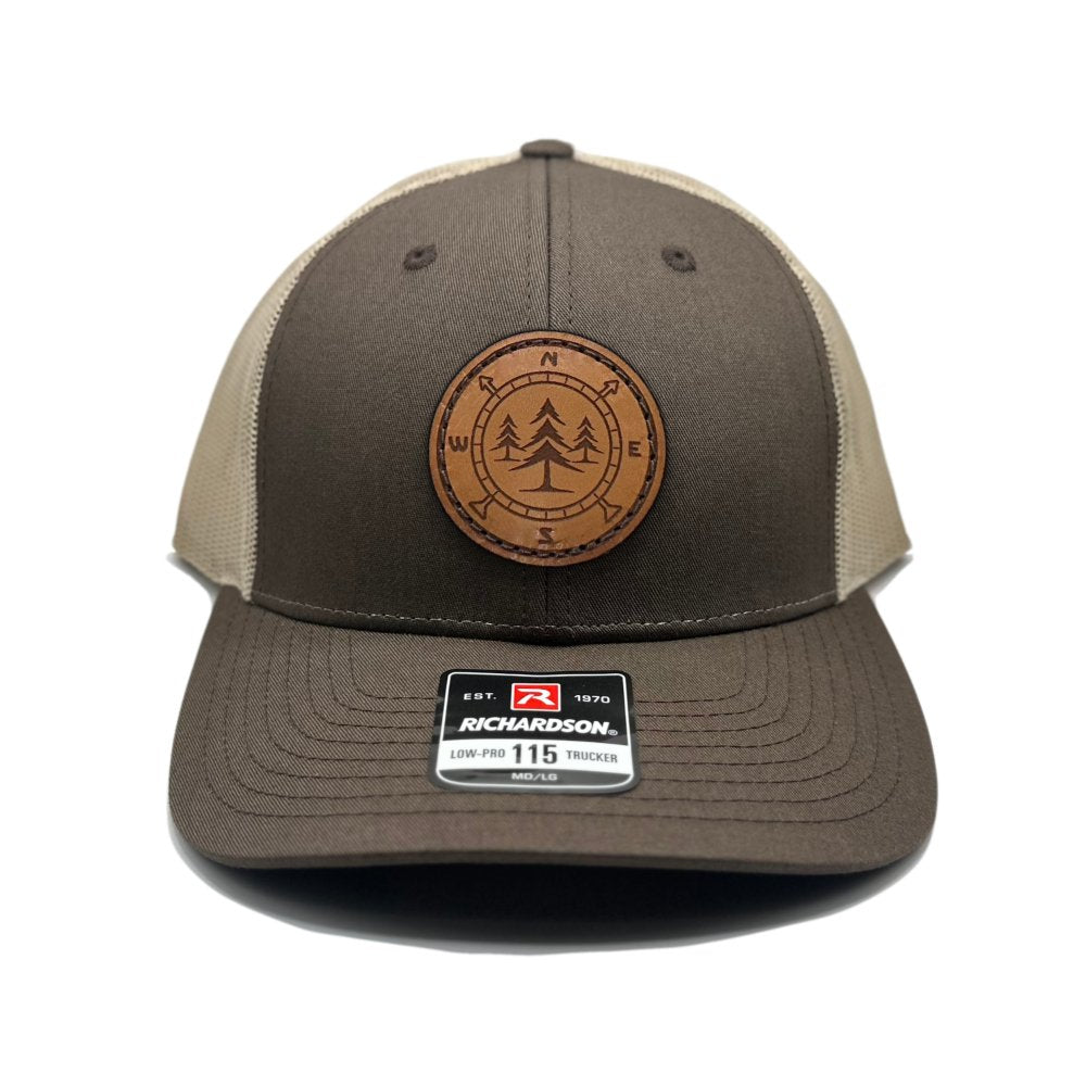 Front view of the Lost Pine Hat in Brown/Khaki by Outer Wings, displaying a circle-shaped leather patch with a compass and pine trees design. This hat is built on the Richardson 115 Low Profile Hat, featuring a structured six-panel, mid-profile design with an adjustable snapback.