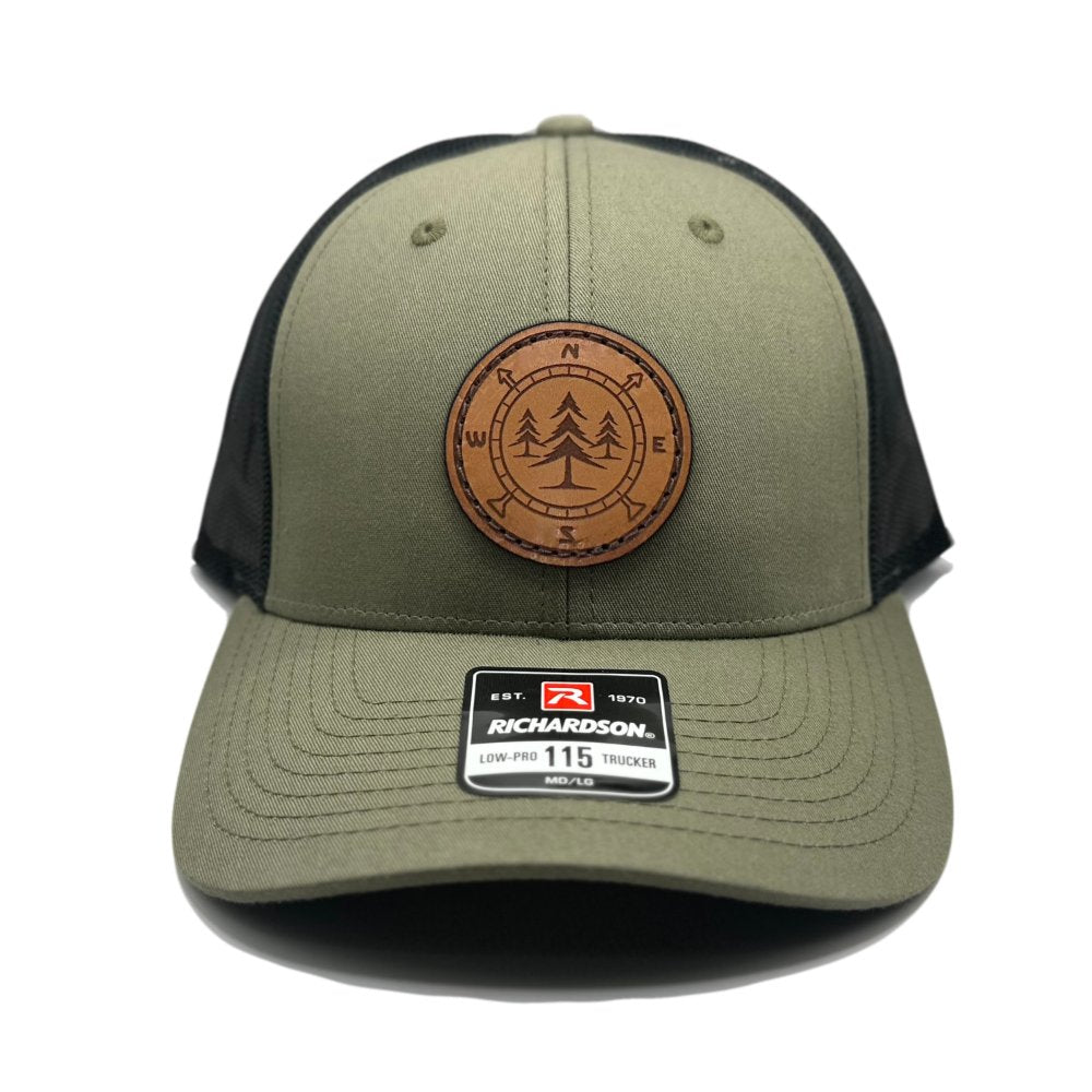 Front view of the Lost Pine Hat in Loden/Black by Outer Wings, featuring a unique circle-shaped leather patch with a compass and pine trees design. The Richardson 115 Low Profile Hat offers a comfortable fit with a structured six-panel build and adjustable snapback closure.