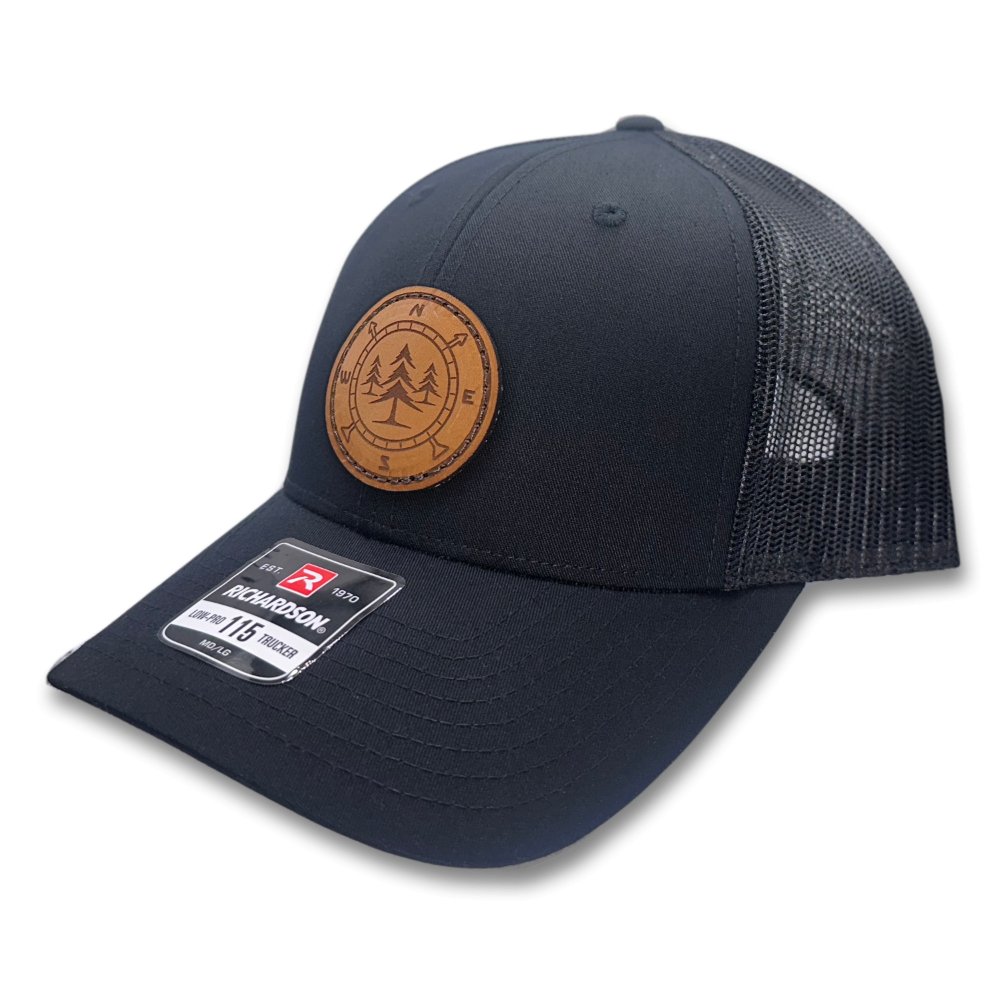 Side view of the Lost Pine Hat in Black/Black, highlighting the structured low-profile, six-panel design, and breathable mesh back. The hat features a hand-stitched leather patch with a compass and pine trees design, perfect for outdoor enthusiasts.