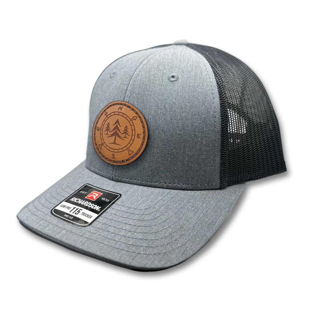 Side view of the Lost Pine Hat in Heather Grey/Dark Charcoal, highlighting the breathable mesh back, structured profile, and pre-curved visor. The hat includes a hand-stitched leather patch with a compass and pine trees design, perfect for outdoor adventures.