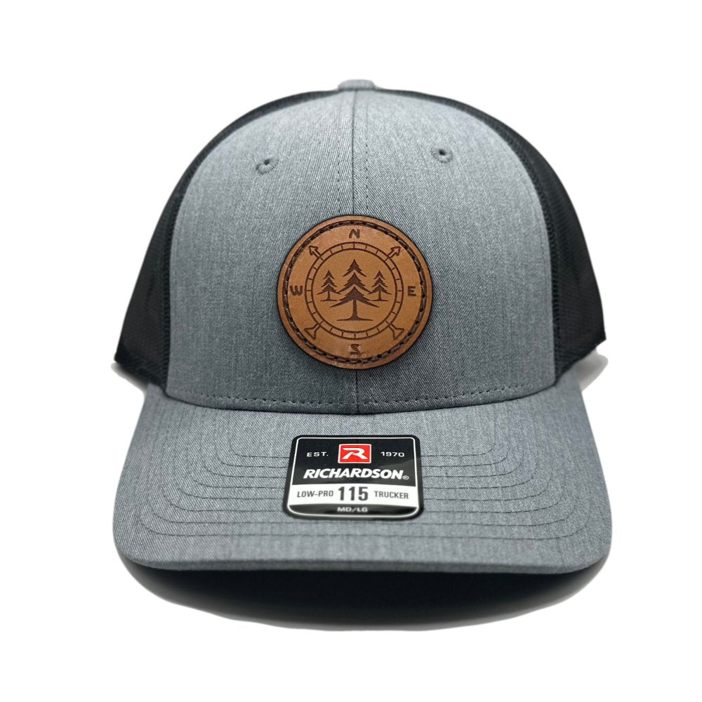 Front view of the Lost Pine Hat in Heather Grey/Dark Charcoal by Outer Wings, featuring a hand-stitched circle-shaped leather patch with a compass and pine trees design. Crafted on the Richardson 115 Low Profile Hat, it offers a structured six-panel design with an adjustable snapback closure.