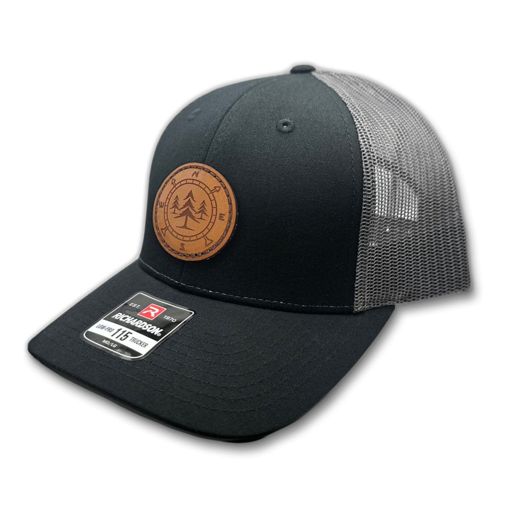 Side view of the Lost Pine Hat in Black/Charcoal, featuring the structured low-profile design, pre-curved visor, and breathable mesh back. The leather patch with a compass and pine trees design is hand-stitched for a durable and authentic look.