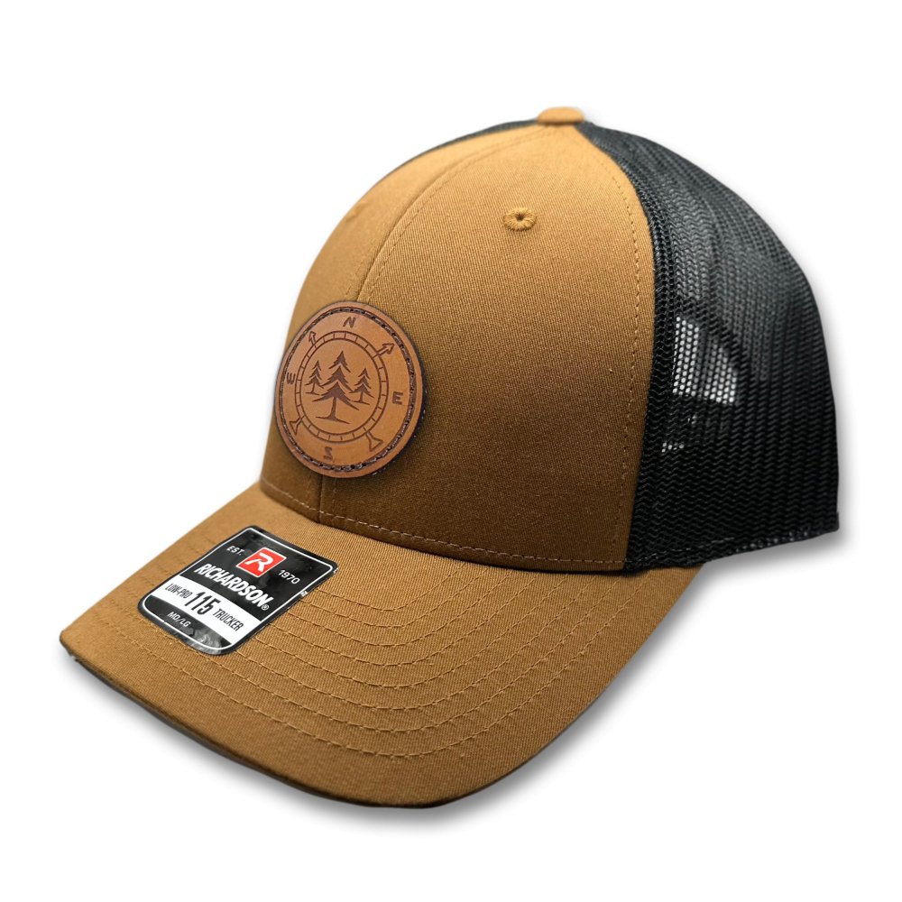 Side view of the Lost Pine Hat in Caramel/Black, showcasing the breathable mesh back, structured profile, and adjustable closure. The hat includes a hand-stitched leather patch with a compass and pine trees design, perfect for those who love the outdoors.